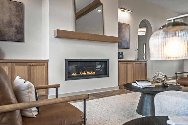 living room featuring vaulted ceiling, arched walkways, dark wood finished floors, and a glass covered fireplace