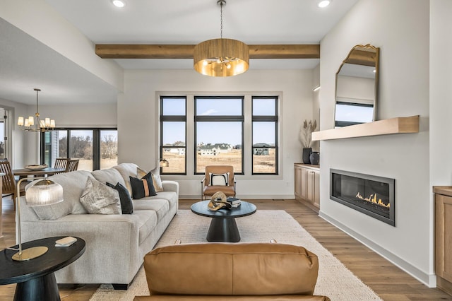 living area with light wood-style floors, a glass covered fireplace, beam ceiling, and an inviting chandelier