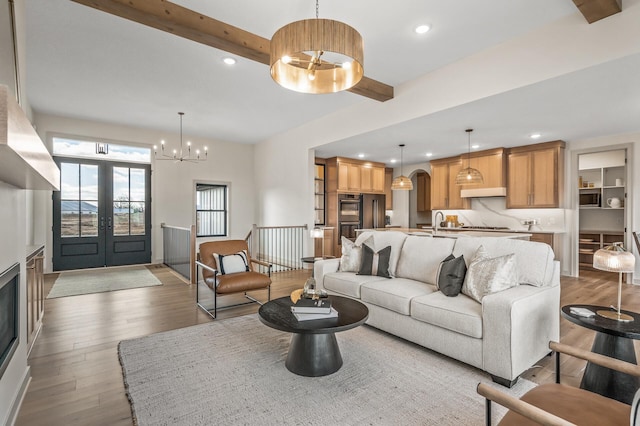 living area with light wood finished floors, beamed ceiling, an inviting chandelier, french doors, and recessed lighting