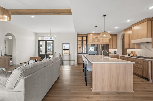 kitchen featuring open floor plan, stainless steel appliances, light wood finished floors, and arched walkways