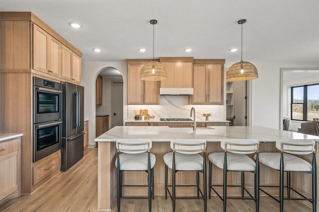 kitchen featuring light wood-style flooring, light brown cabinetry, double oven, high end black refrigerator, and a sink