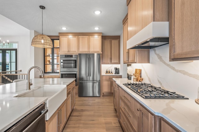 kitchen featuring light stone counters, pendant lighting, appliances with stainless steel finishes, a sink, and light wood-type flooring