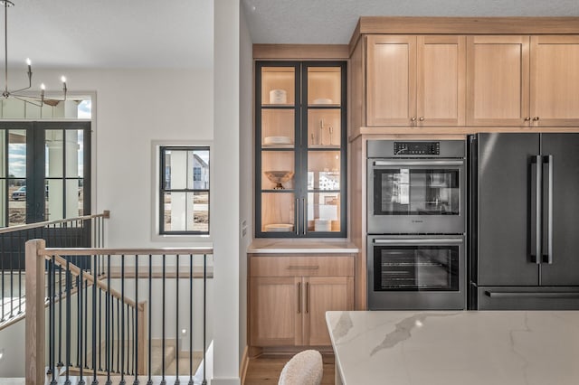 kitchen with light stone counters, freestanding refrigerator, stainless steel double oven, wood finished floors, and a chandelier