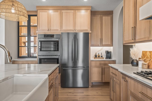 kitchen with stainless steel appliances, wood finished floors, a sink, ventilation hood, and pendant lighting