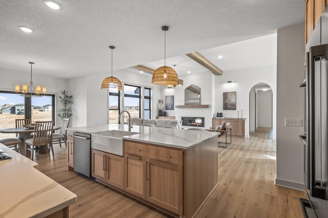 kitchen with a warm lit fireplace, brown cabinetry, dishwasher, light wood-style flooring, and a sink