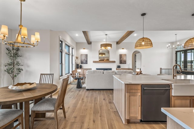 kitchen featuring arched walkways, a sink, stainless steel dishwasher, light wood-type flooring, and beamed ceiling