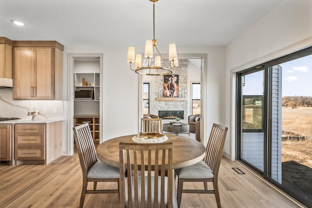 dining room featuring a stone fireplace, a notable chandelier, and light wood-style flooring