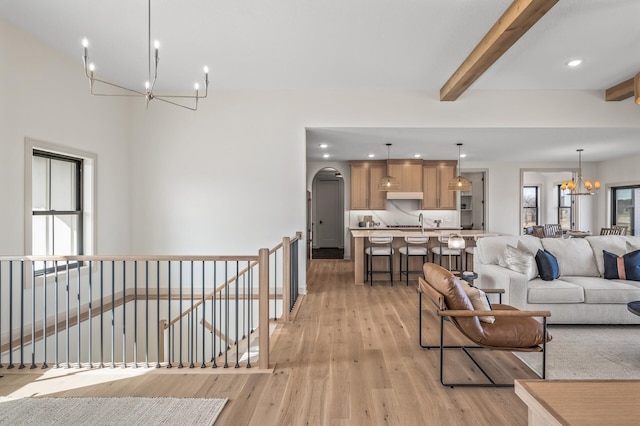 living area featuring a chandelier, light wood finished floors, beamed ceiling, and arched walkways