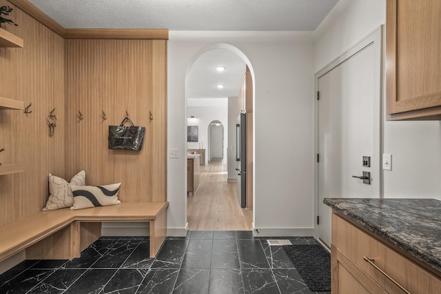 mudroom with arched walkways, marble finish floor, a textured ceiling, and baseboards