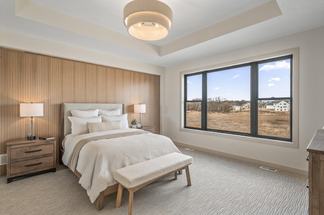 bedroom featuring light carpet, visible vents, a tray ceiling, and baseboards