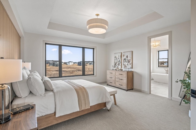 bedroom with a raised ceiling, light carpet, baseboards, and ensuite bathroom