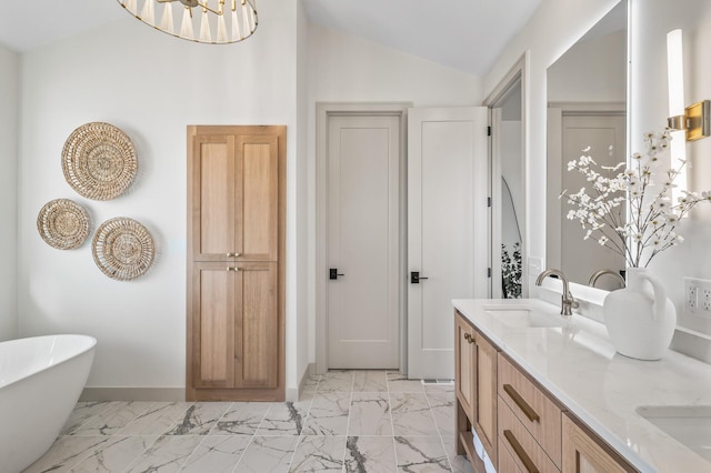 bathroom with marble finish floor, lofted ceiling, a freestanding bath, a sink, and baseboards