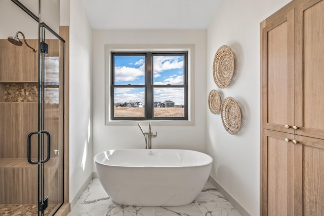 full bath featuring marble finish floor, a freestanding tub, a shower stall, and baseboards