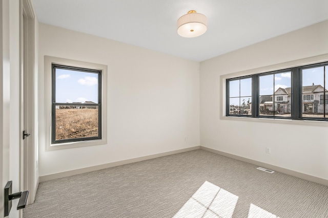 empty room with carpet, visible vents, and baseboards