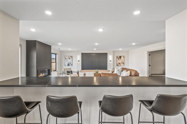 kitchen with a glass covered fireplace, a peninsula, dark countertops, and recessed lighting