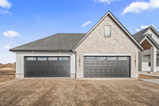 view of front of home with a garage, a shingled roof, stone siding, an outbuilding, and board and batten siding