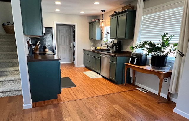 kitchen with dishwasher, dark countertops, a sink, and light wood-style flooring