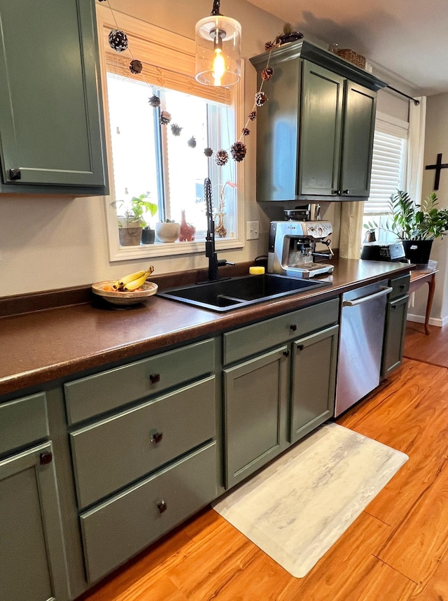 kitchen with decorative light fixtures, dark countertops, stainless steel dishwasher, a sink, and light wood-type flooring