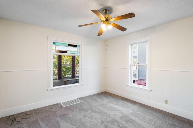 carpeted empty room with a wainscoted wall, a ceiling fan, visible vents, and a textured ceiling