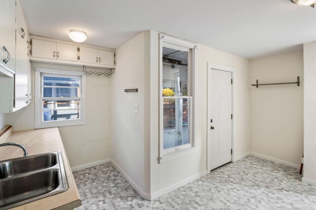 kitchen with light countertops, white cabinets, a sink, and baseboards