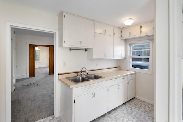 kitchen with light countertops, light colored carpet, a sink, and baseboards