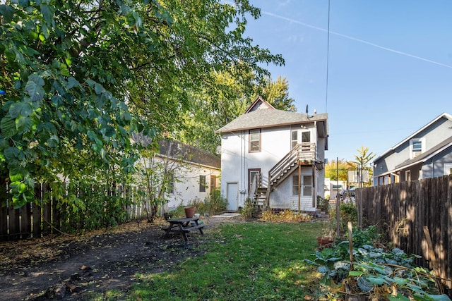 rear view of house with a yard, stairs, fence, and stucco siding