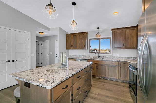 kitchen featuring light stone counters, a center island, electric range oven, freestanding refrigerator, and a sink