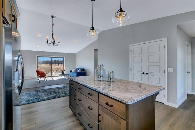 kitchen featuring light stone counters, vaulted ceiling, stainless steel refrigerator with ice dispenser, and wood finished floors