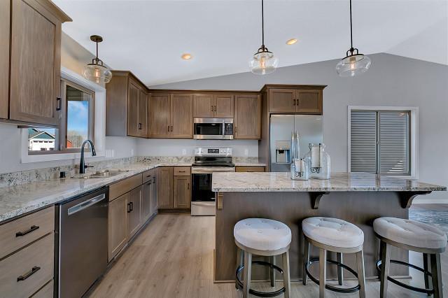 kitchen featuring light wood finished floors, light stone counters, a breakfast bar, stainless steel appliances, and a sink