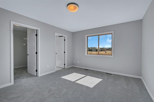 unfurnished bedroom featuring carpet floors, a walk in closet, visible vents, and baseboards