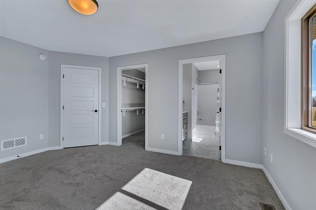 unfurnished bedroom with carpet, visible vents, ensuite bath, and baseboards