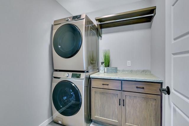 washroom featuring cabinet space, baseboards, and stacked washer and clothes dryer