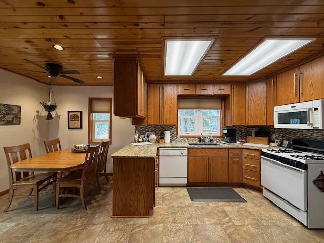 kitchen featuring white appliances, decorative backsplash, wooden ceiling, brown cabinets, and a sink