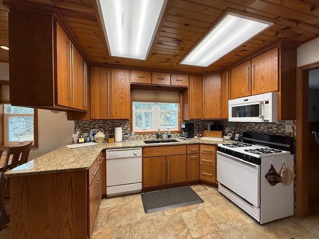 kitchen with white appliances, a sink, wood ceiling, brown cabinets, and tasteful backsplash