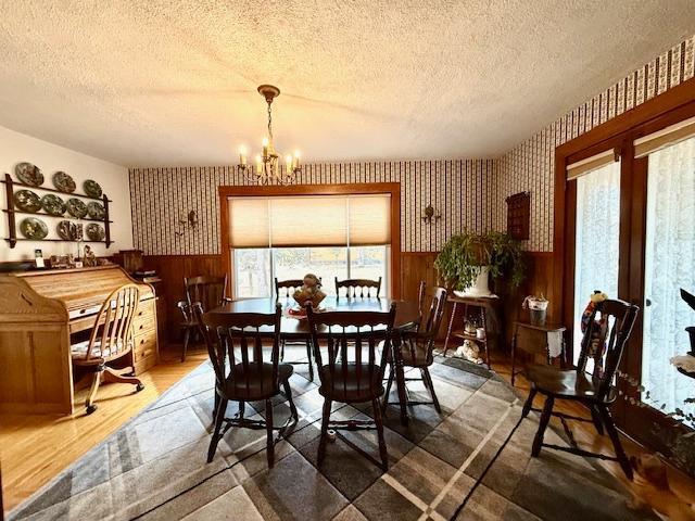 dining space with a chandelier, a textured ceiling, wainscoting, and wallpapered walls