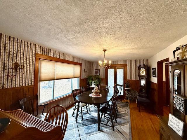 dining room with wainscoting, a notable chandelier, a textured ceiling, and wallpapered walls