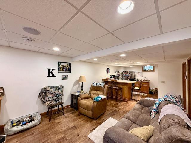 living room featuring a paneled ceiling, recessed lighting, indoor bar, wood finished floors, and baseboards