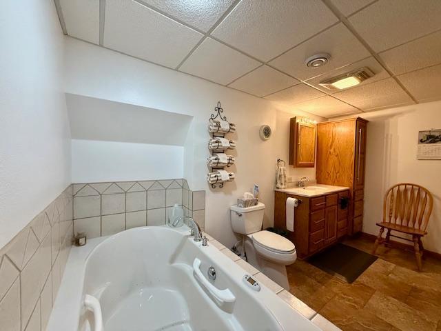 full bathroom featuring visible vents, a drop ceiling, toilet, a garden tub, and vanity