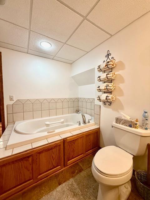 full bathroom featuring a drop ceiling, a garden tub, and toilet