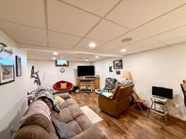 living area with baseboards, wood finished floors, a paneled ceiling, and recessed lighting