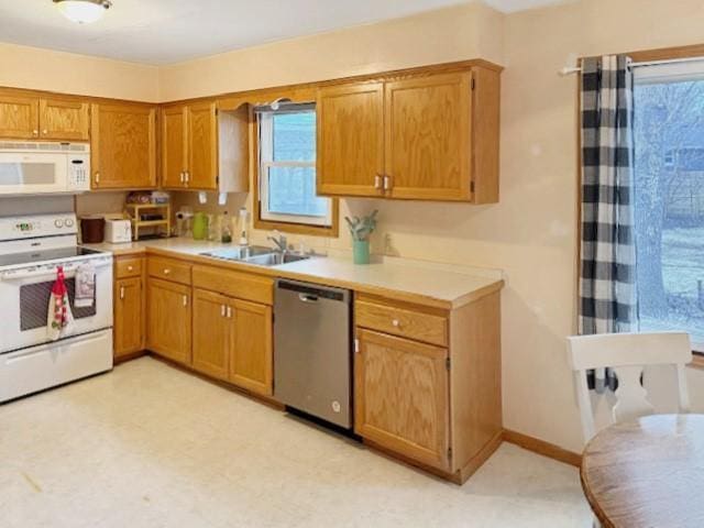 kitchen featuring light floors, light countertops, brown cabinetry, white appliances, and a sink