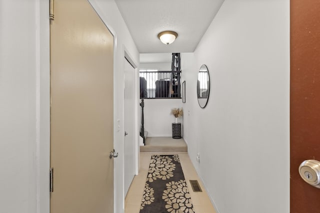 hall featuring a textured ceiling, light tile patterned flooring, visible vents, and baseboards