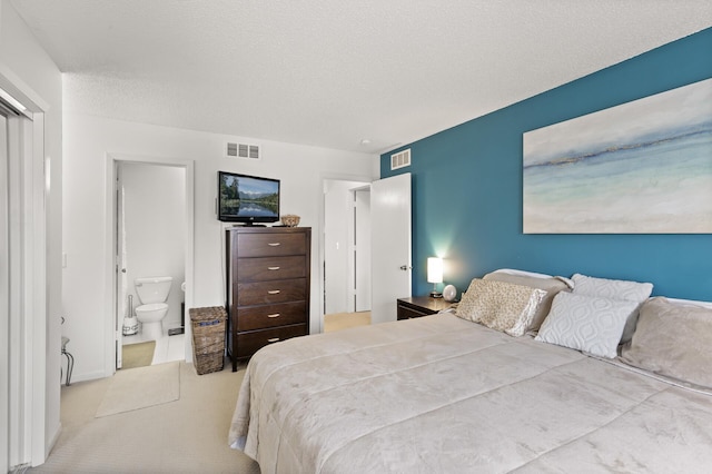 bedroom featuring connected bathroom, visible vents, and a textured ceiling