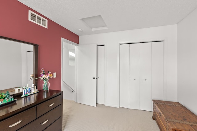 bedroom with a textured ceiling, light colored carpet, visible vents, and attic access