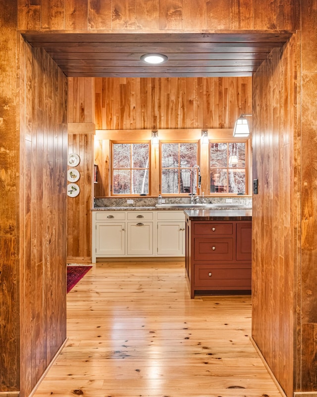 kitchen featuring wood walls, white cabinetry, light wood-type flooring, a sink, and healthy amount of natural light