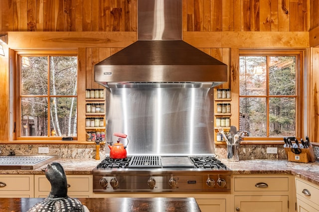 kitchen featuring wall chimney exhaust hood, backsplash, light stone counters, and stainless steel gas cooktop