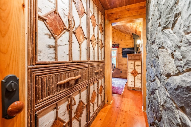hallway with wooden walls, wooden ceiling, vaulted ceiling, and light wood-style flooring