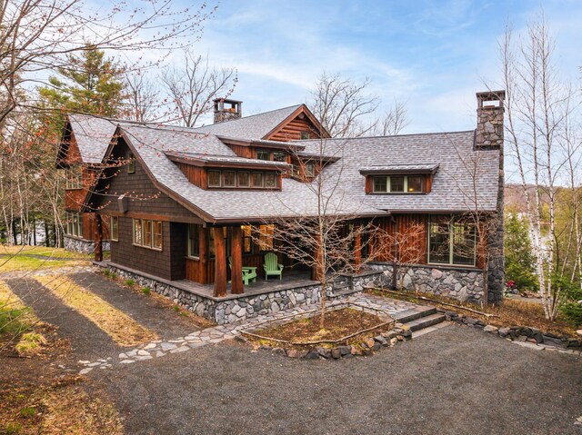 view of front of property featuring a chimney, roof with shingles, stone siding, and a patio area