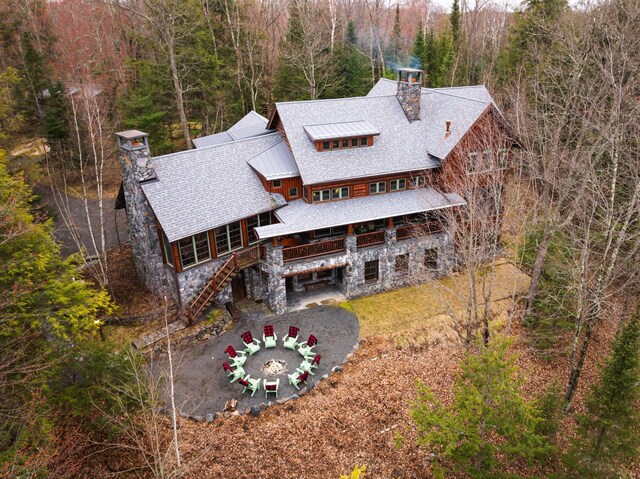 rear view of house with a chimney, a fire pit, stairs, a forest view, and stone siding