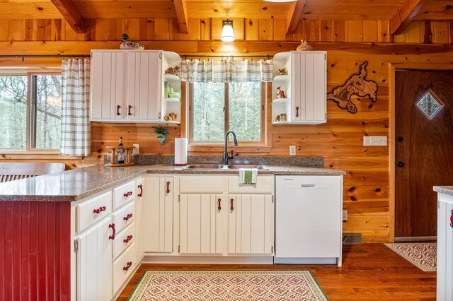 kitchen featuring open shelves, a sink, white dishwasher, beam ceiling, and wood walls